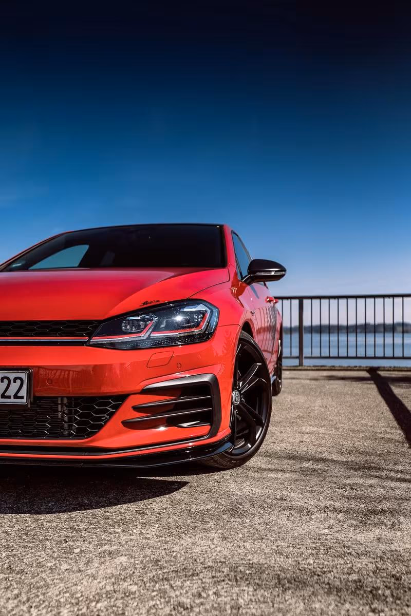 Volkswagen: Roter VW Golf GTI mit schwarzem Frontspoiler vor Wasser und Geländer