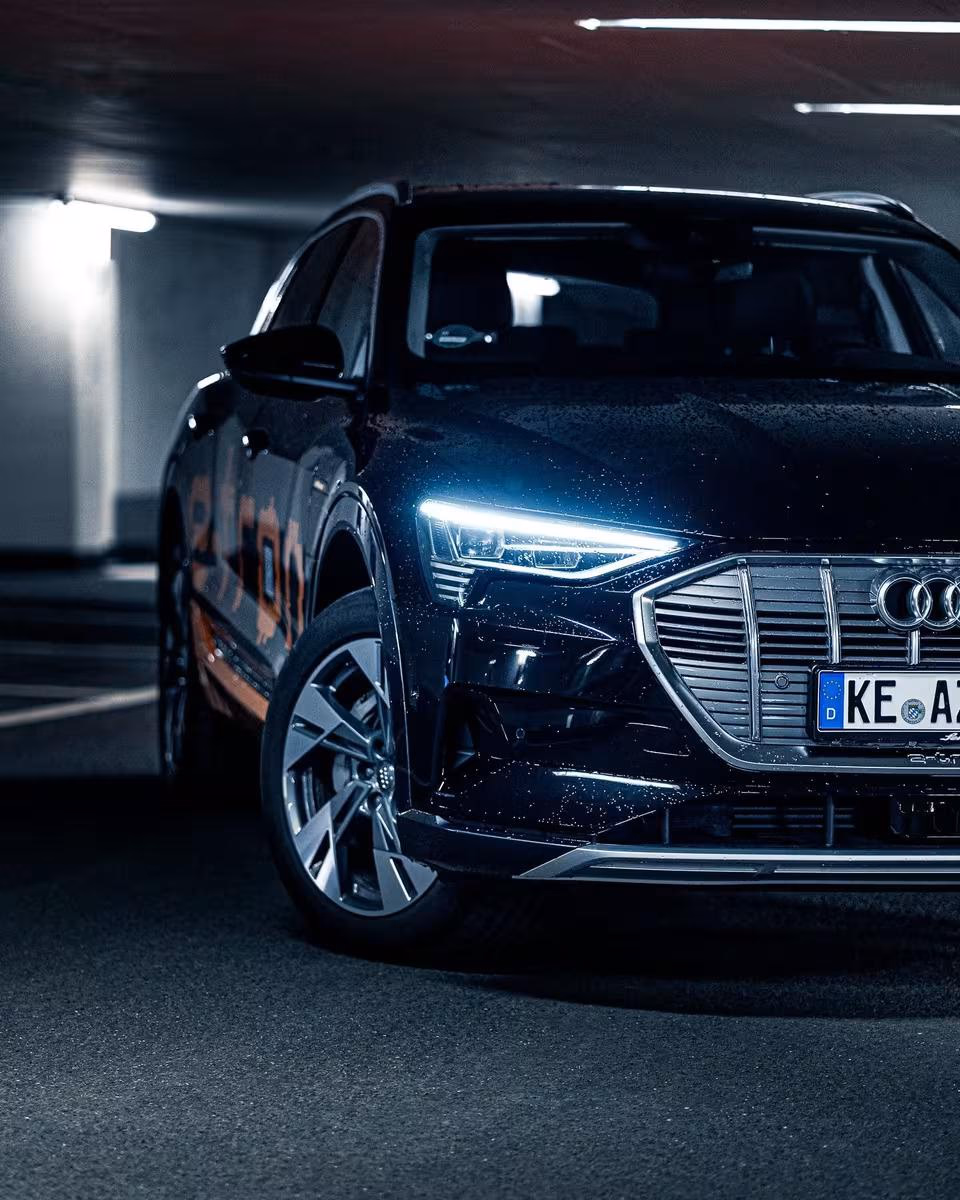 Black Audi e-tron with active LED headlights parked in a lit underground garage.