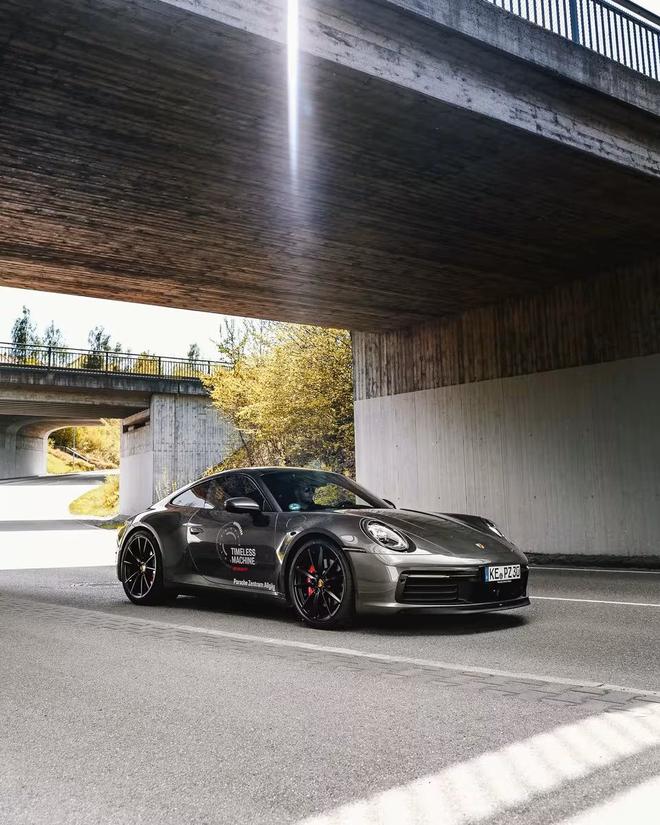 Grauer Porsche 911 Carrera 4S mit „Timeless Machine“-Decal unter einer Brücke.