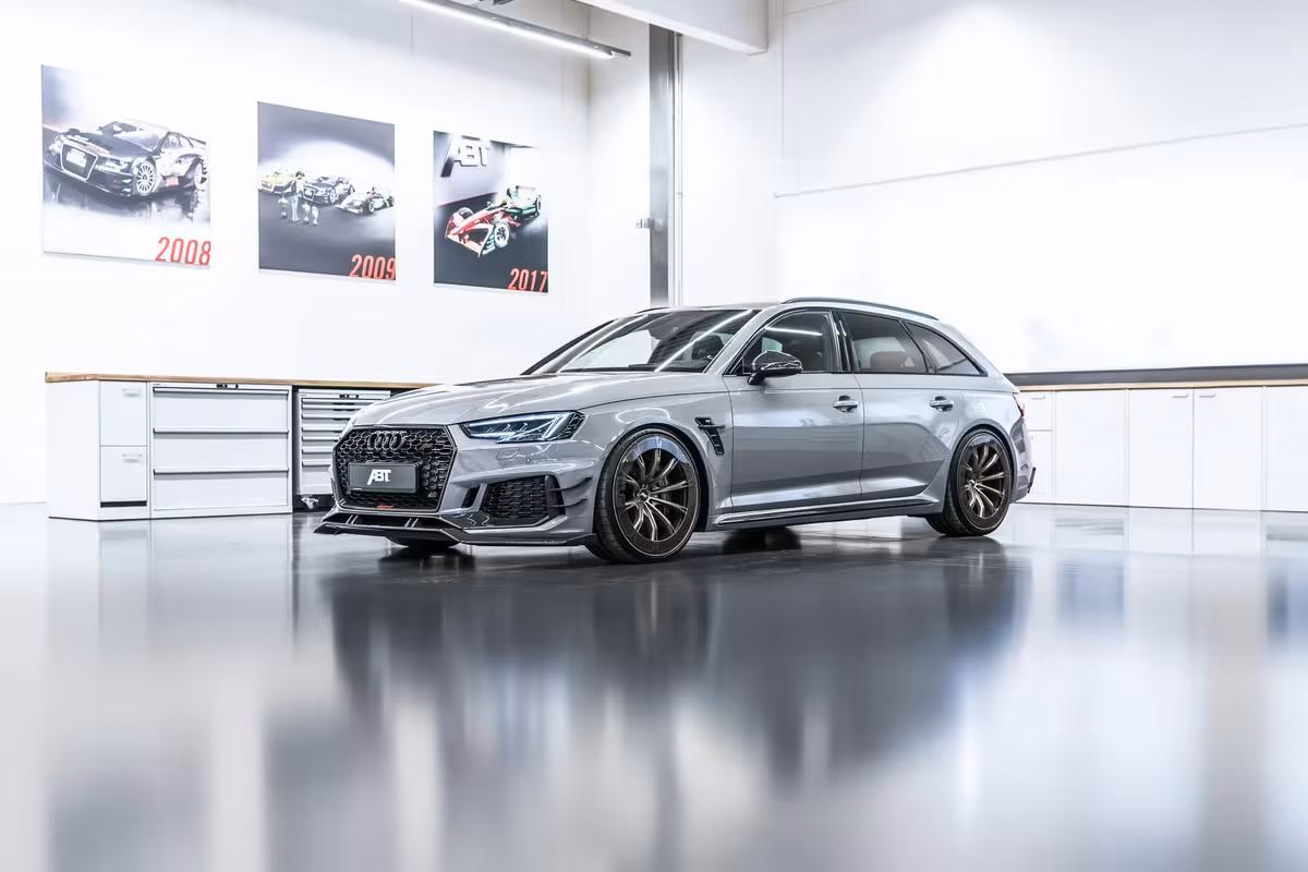 Grauer Audi RS6 Avant von ABT im hellen Studio mit historischen Rennwagen-Postern an der Wand.