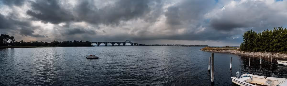 Copenhagen: Panorama einer Flusslandschaft mit Brücke, Booten und bewölktem Himmel.