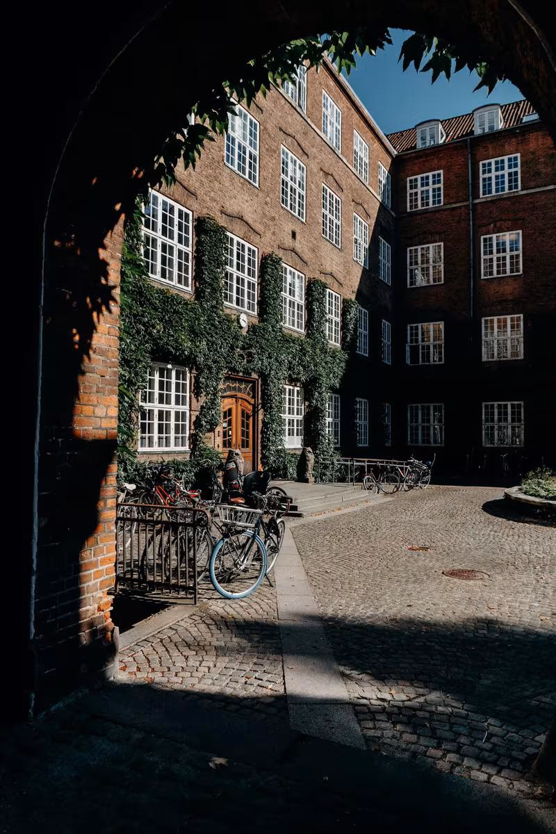 Copenhagen: Blick durch einen Bogen auf einen gepflasterten Innenhof mit Fahrrädern und Backsteinfassade.