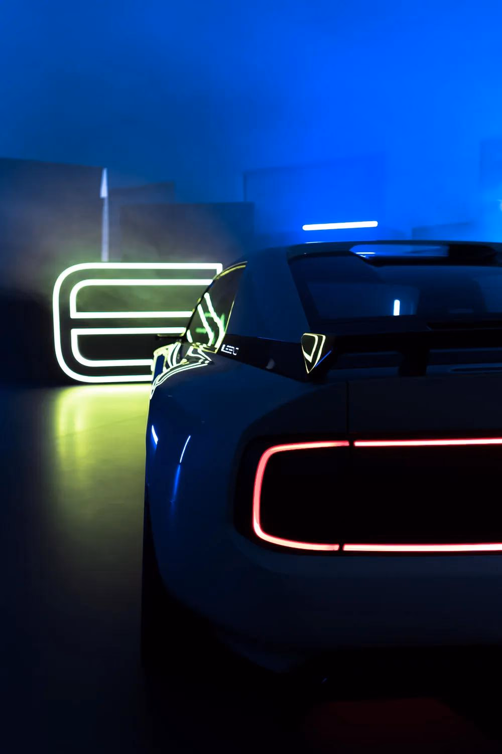Rückansicht eines E-Legend-Sportwagens mit roten Leuchten vor blauem Neonhintergrund.