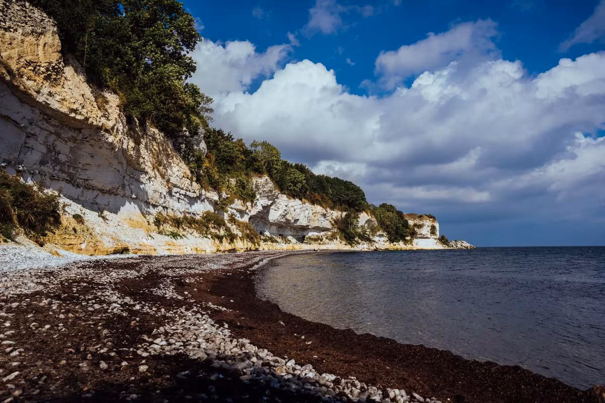 Copenhagen: Küstenklippe mit weißem Fels, dunklem Strand und Meer unter blauem Himmel