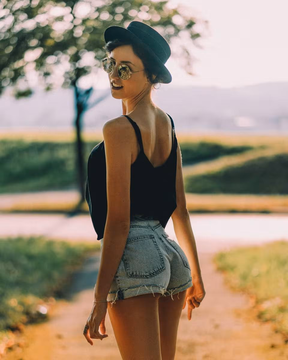Lifestyle: Frau mit Hut und Sonnenbrille lächelt auf einem Feldweg.