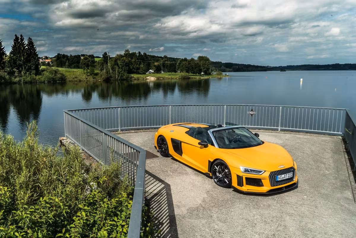 Gelber Audi R8 Spyder auf einer Stegterrasse vor einem See.