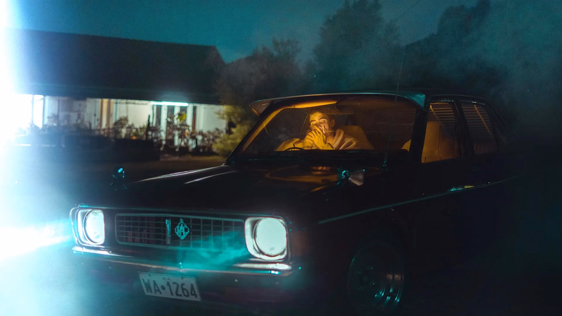 Person in dunklem Oldtimer bei Nacht, beleuchtet von Scheinwerfern und Nebel.