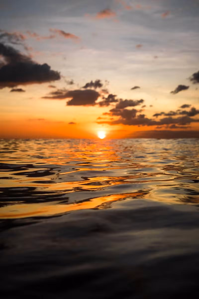 Thailand: Sonnenuntergang über dem Meer mit goldenem Licht und dunklen Wolken.