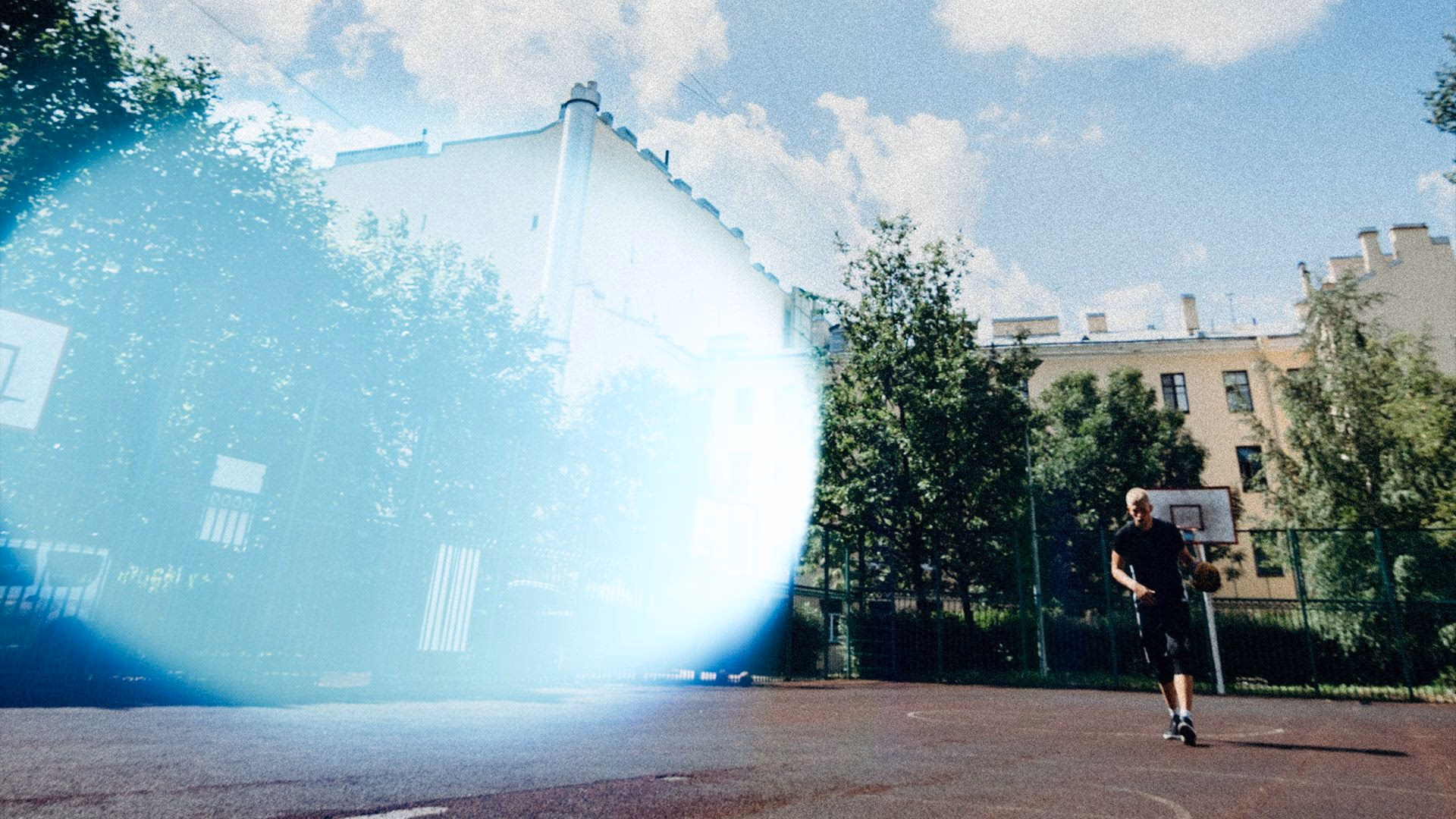 Mann mit Basketball auf einem beleuchteten Außenplatz bei Tageslicht.