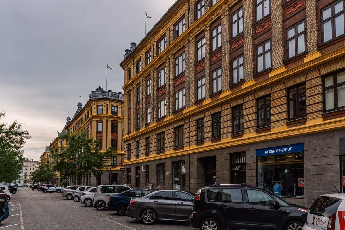 Copenhagen: Historisches Backstein-Gebäude in Kopenhagen mit gelben Fassadenakzenten und geparkten Autos.