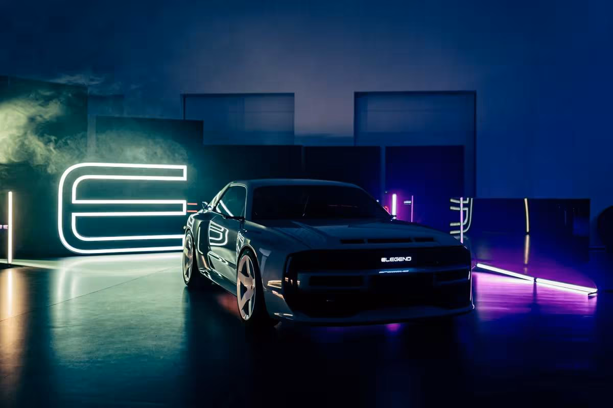 Silberner E-Legend-Sportwagen vor leuchtendem Neon-Logo in dunkler Halle