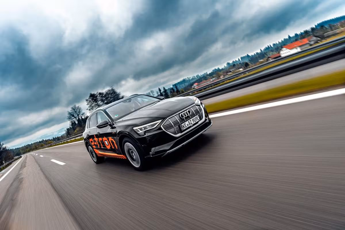 Black Audi e-tron with orange lettering driving on a highway.