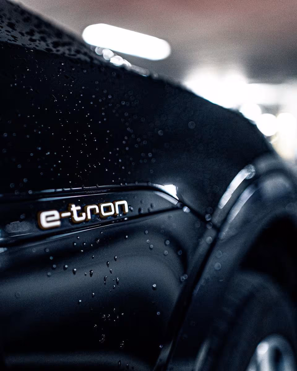Close-up of a wet black car featuring the “e-tron” badge.