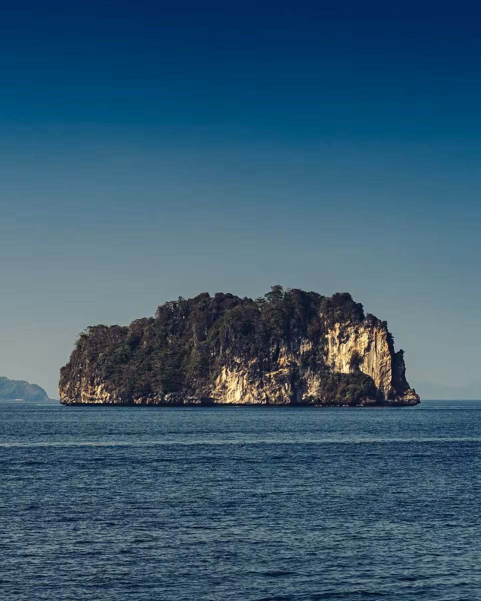 Thailand: Felsige, bewaldete Insel im Meer unter klarem Himmel