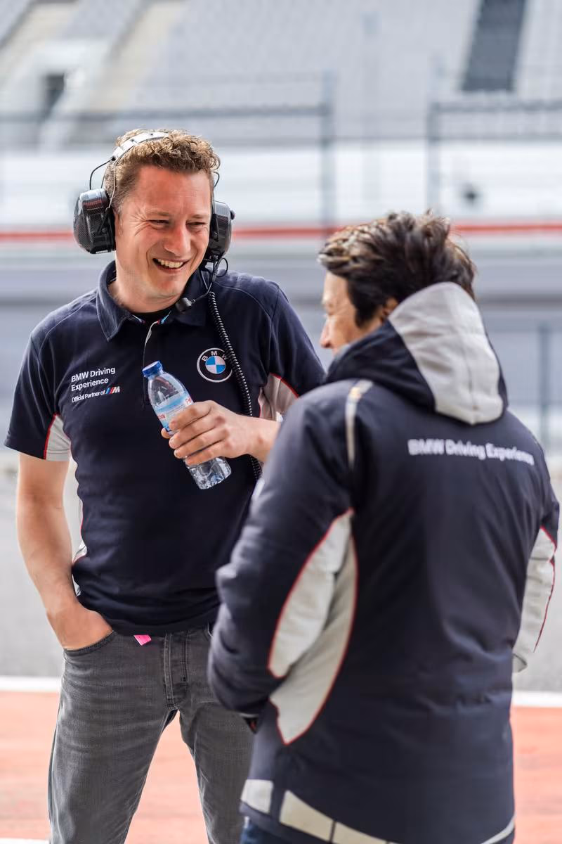 Zwei BMW Driving Experience Mitarbeiter unterhalten sich lachend am Rennstreckeneingang.