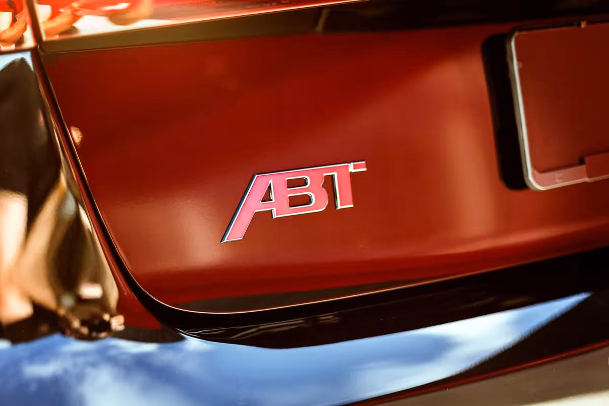 Audi: Rotes Fahrzeugheck mit pinkfarbenem ABT-Emblem und schwarzem Stoßfänger.
