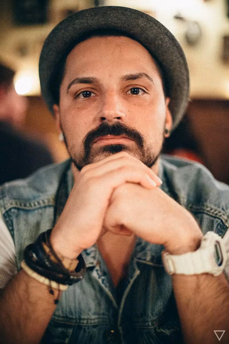 Lifestyle: Mann mit Hut und Bart, verschränkte Hände, Jeansjacke, im Porträt.