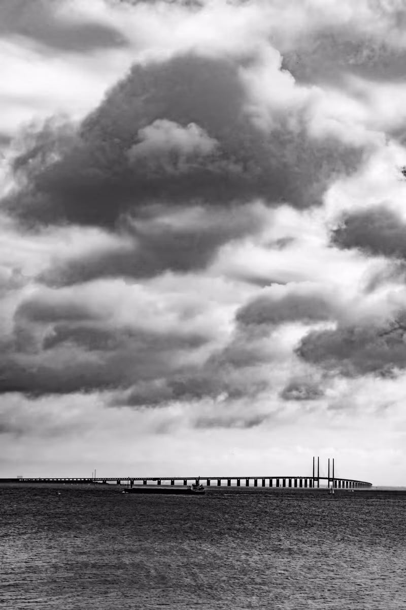 Copenhagen: Schwarz-Weiß-Foto: Himmelslandschaft mit Wolken und Brücke am Horizont