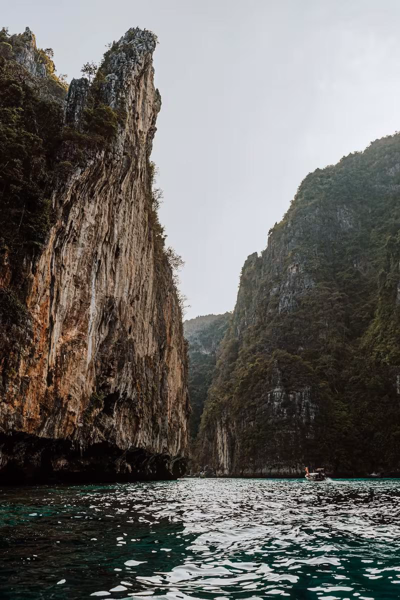 Thailand: Steile Kalkfelsen und ein Boot auf türkisfarbenem Wasser in einer thailändischen Bucht.