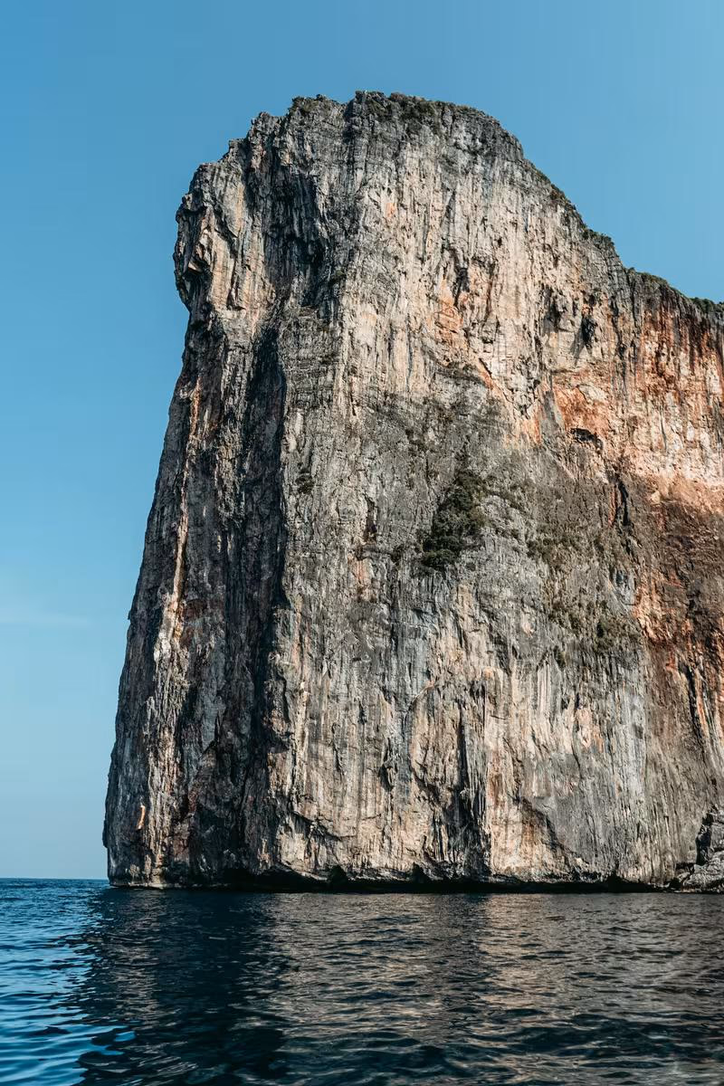 Thailand: Steile Felsklippe im Meer unter klarem blauem Himmel