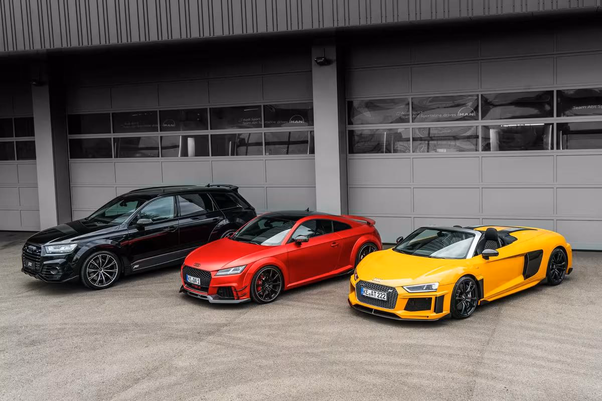 Drei Audi-Modelle in Schwarz, Rot und Gelb vor einer modernen Industriehalle.