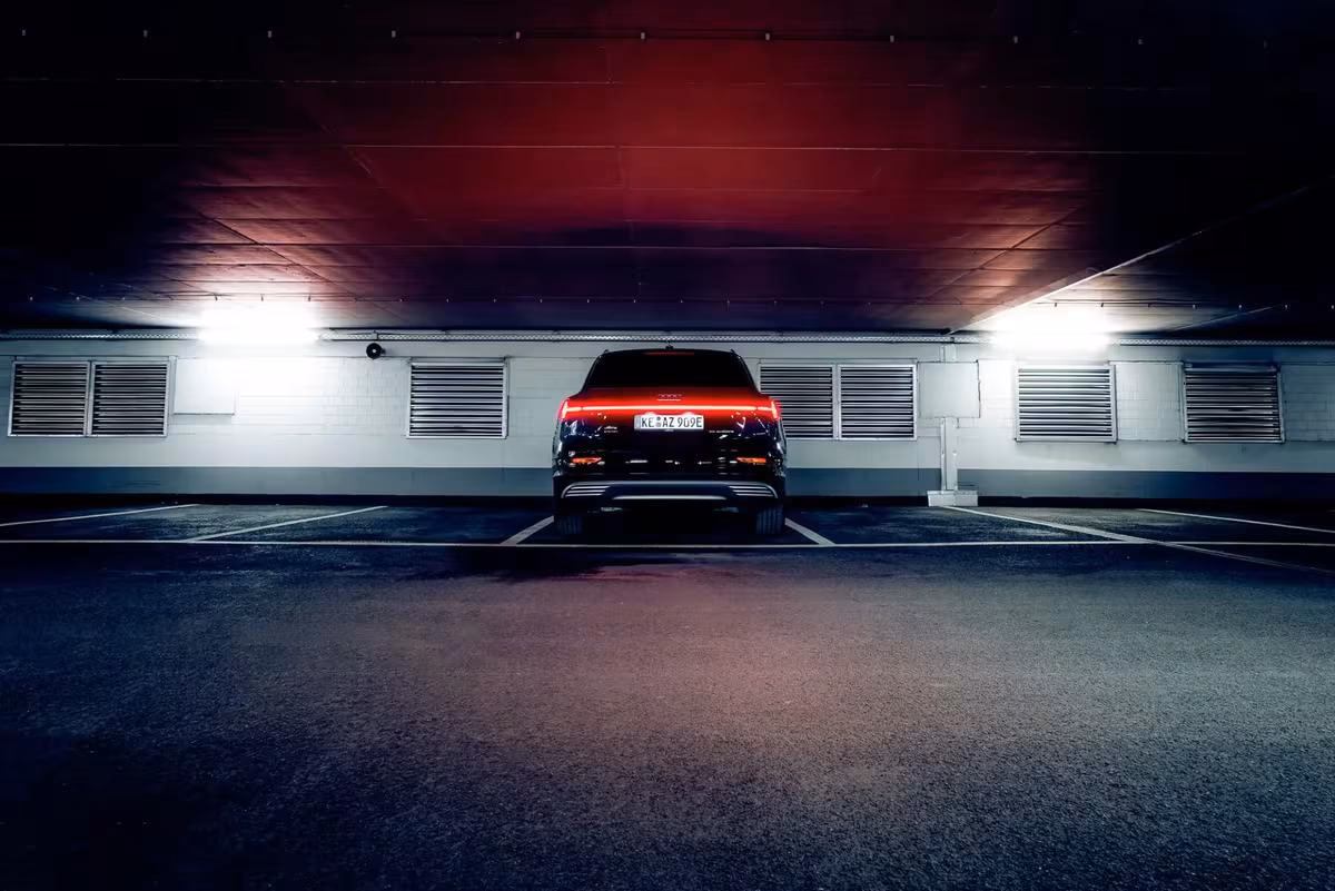 Black Audi E-Tron seen from behind in a dimly lit underground garage with red lighting.