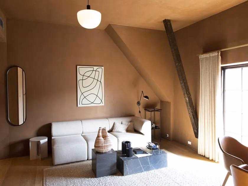 Axor: Wohnzimmer mit weißem Sofa, dunklem Marmortisch und abgerundetem Spiegel an erdigen Wänden.