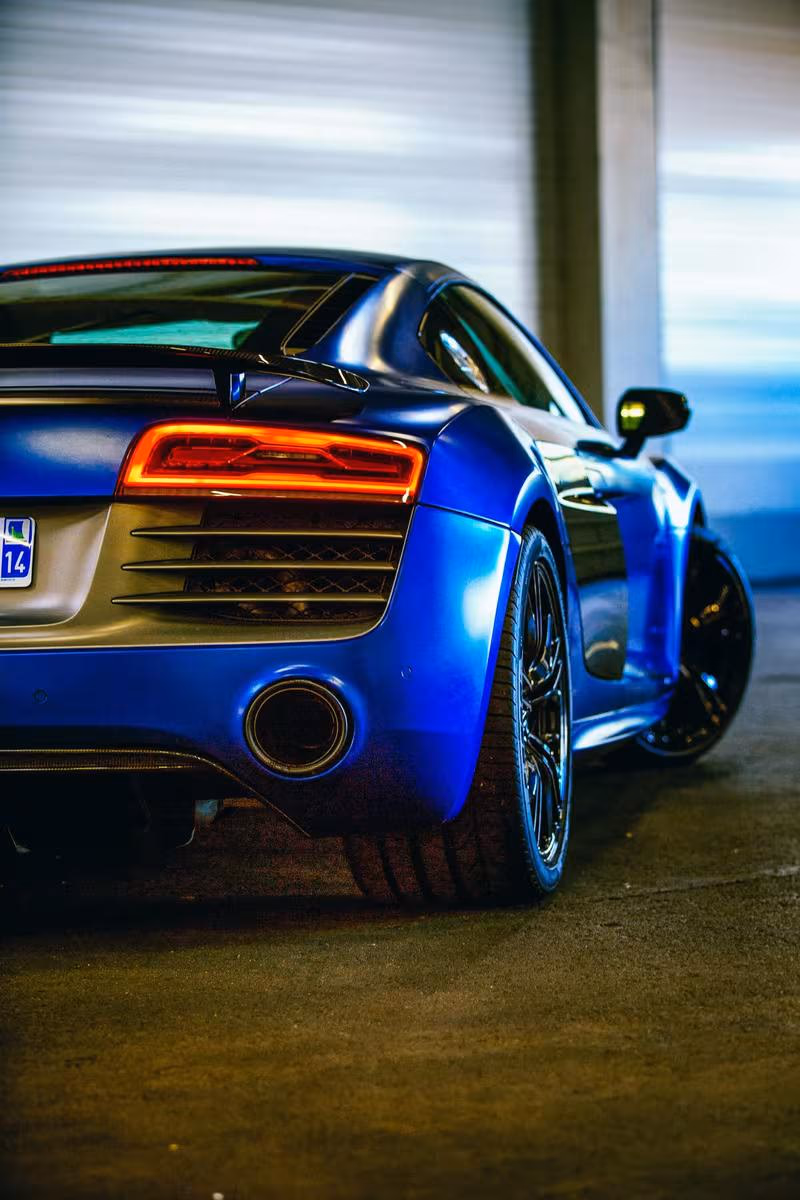 Audi: Blauer Sportwagen mit leuchtenden Rücklichtern und Carbon-Spoiler im Innenraum.