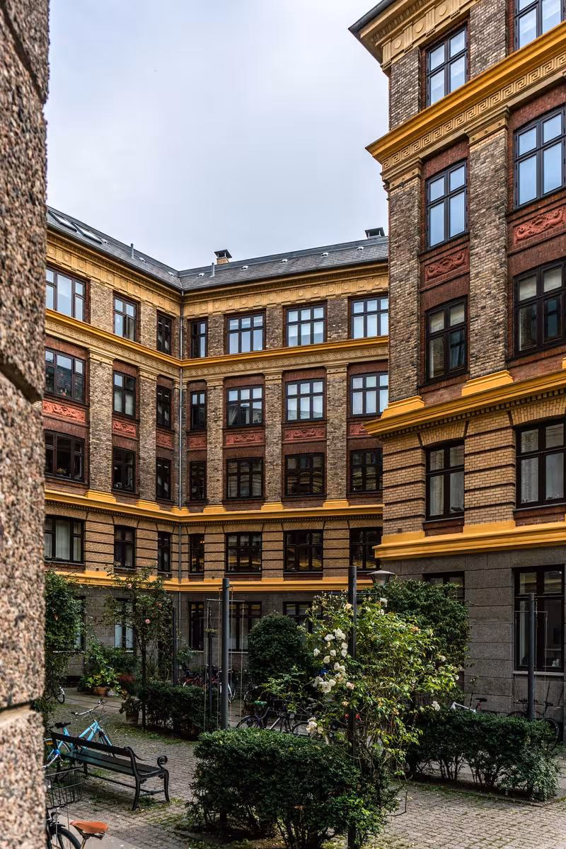 Copenhagen: Historischer Innenhof mit Backsteinfassade, gelben Akzenten und grünen Pflanzen.