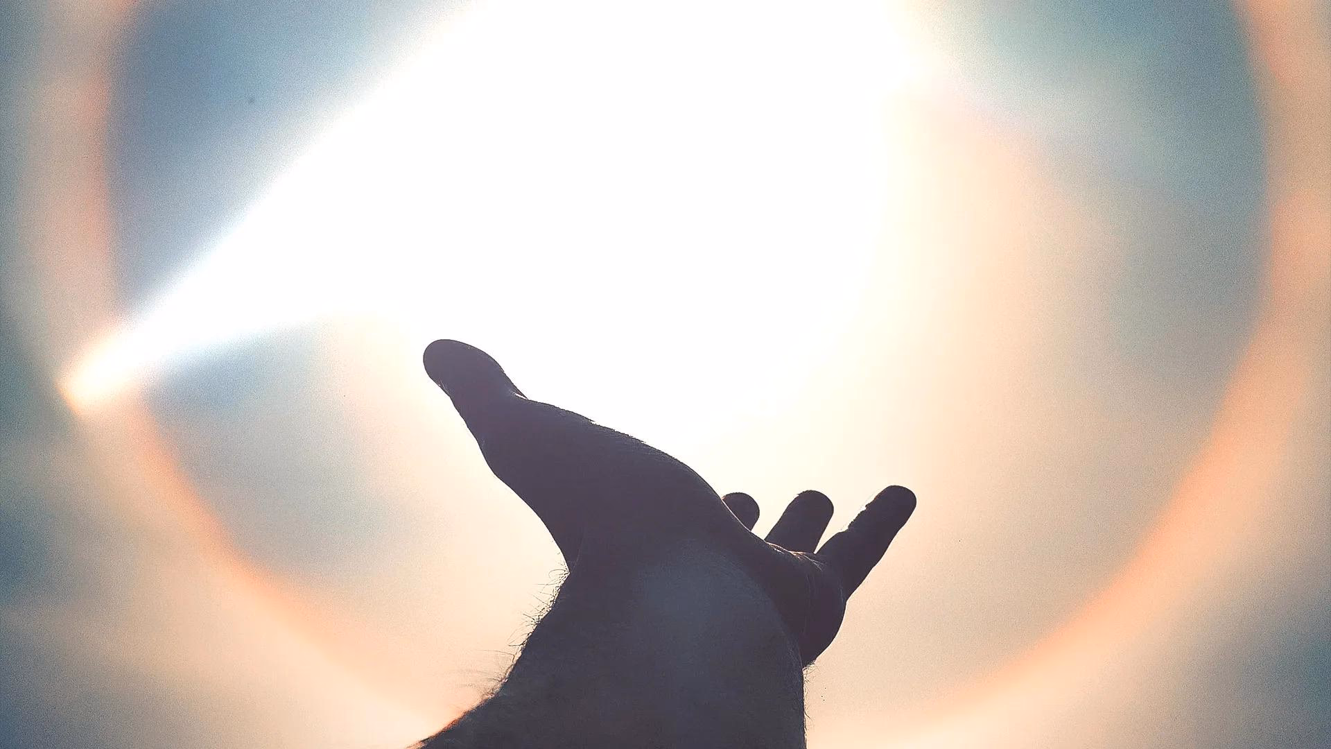 Silhouetted hand blocking the bright sun in the sky.