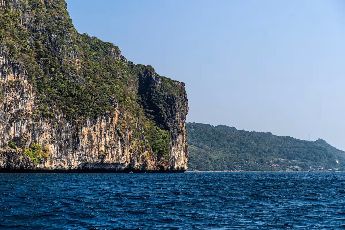 Thailand: Steile, bewachsene Klippe am Meer mit weiter Küstenlandschaft im Hintergrund.