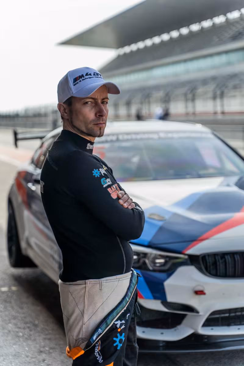 BMW Motorsport: Rennfahrer in BMW-Racing-Outfit vor weißem BMW M4 GT3 auf der Strecke.