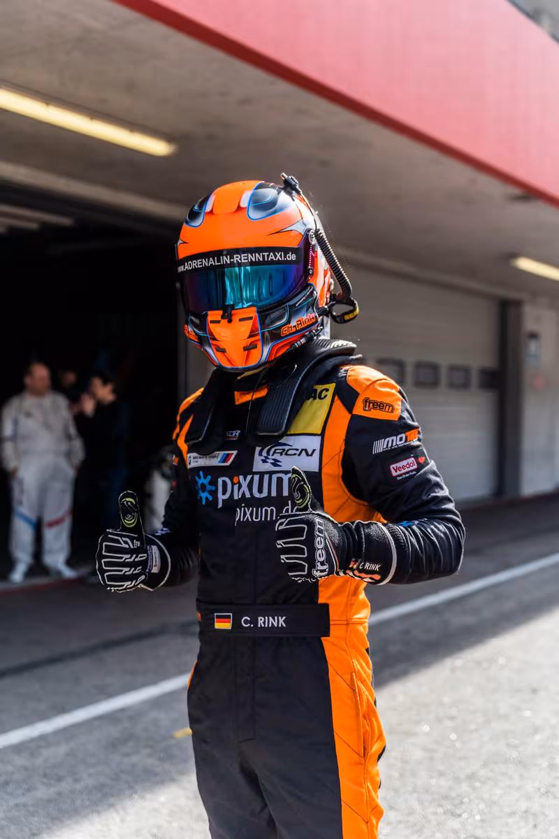 BMW Motorsport: Rennfahrer C. Rink in orange-schwarzem Overalls und Helm mit Daumen hoch