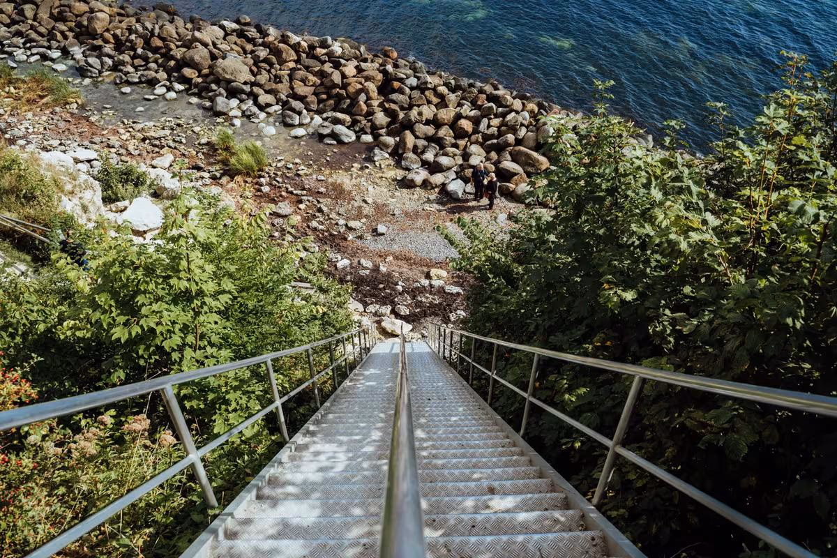 Copenhagen: Metalltreppe führt durch grüne Vegetation hinab zu einem steinigen Ufer am Wasser.