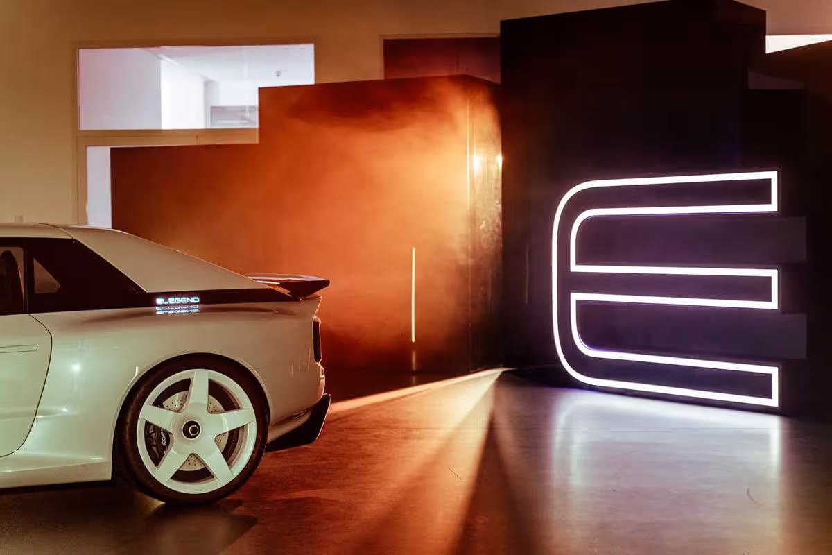 E-Legend-Sportwagen neben großem leuchtendem Logo in dunkler Halle