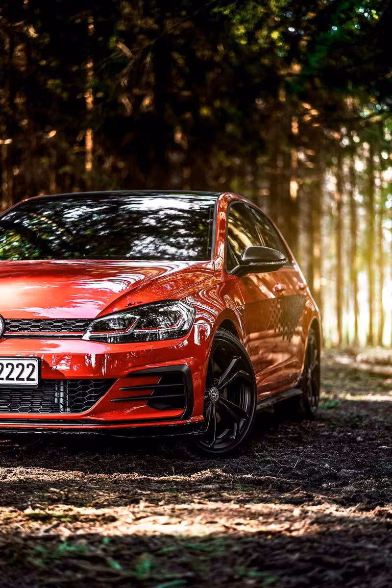 Volkswagen: Roter VW Golf GTI mit schwarzen Felgen auf einem Waldweg