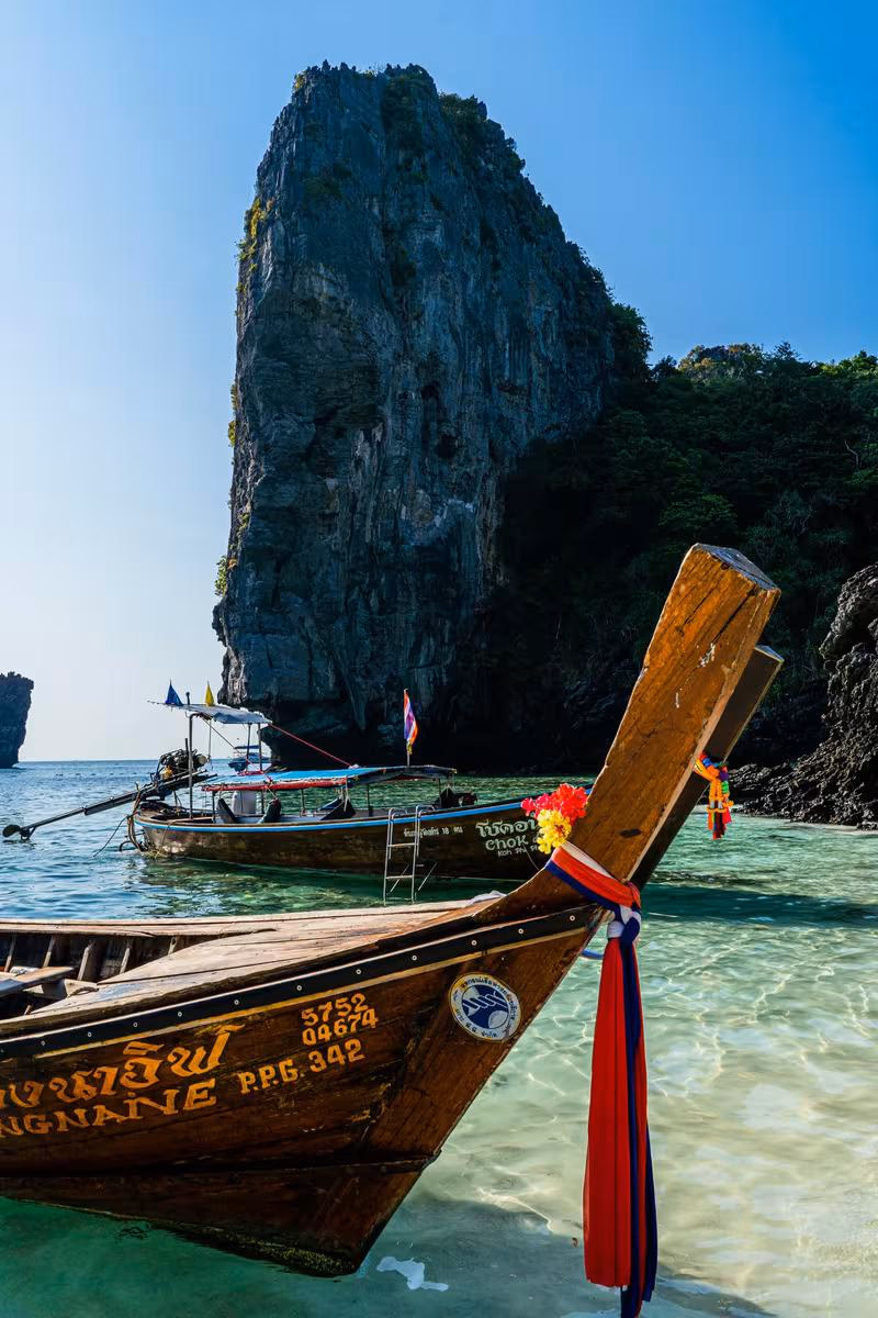 Thailand: Thailändische Longtail-Boote vor einer steilen Kalksteinfelswand in türkisfarbenem Wasser.