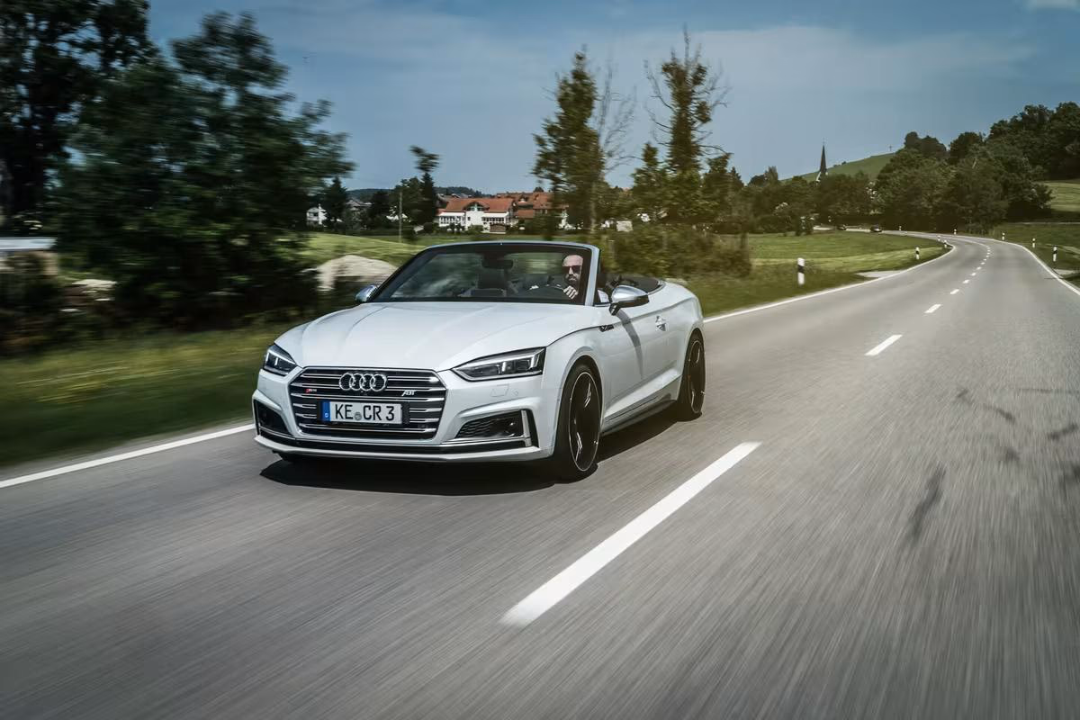 Weißer Audi A5 Cabriolet fährt auf einer Landstraße durch die Landschaft.