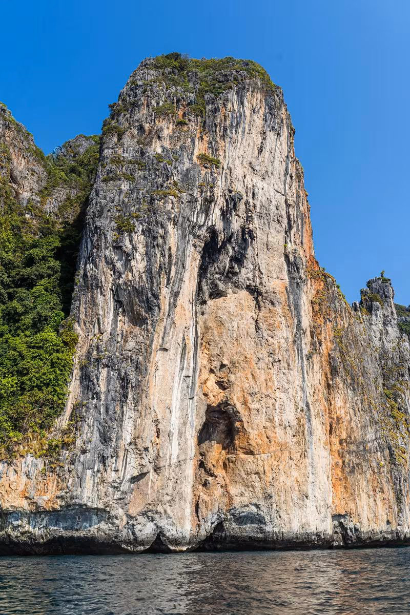 Thailand: Steile Kalksteinfelsen mit Vegetation am Wasser unter blauem Himmel
