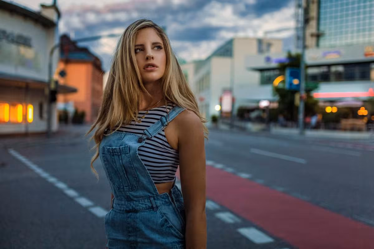 Lifestyle: Blonde Frau in Jeans-Overalls und gestreiftem Top auf einer Stadtstraße