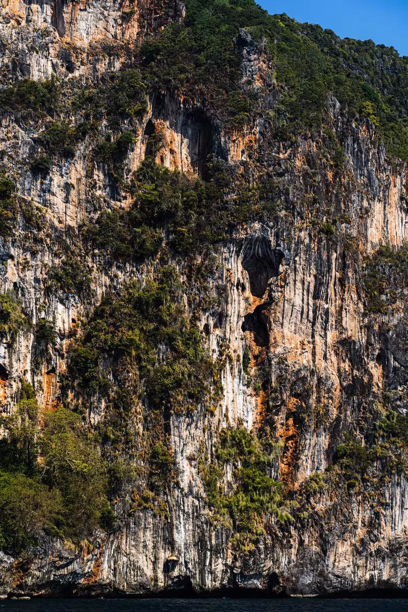 Thailand: Steile, bewachsene Felsklippe mit Höhle über dem Meer