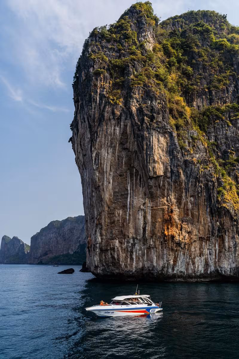 Thailand: Motorboot vor steiler, bewachsener Kalksteinfelswand im thailändischen Meer
