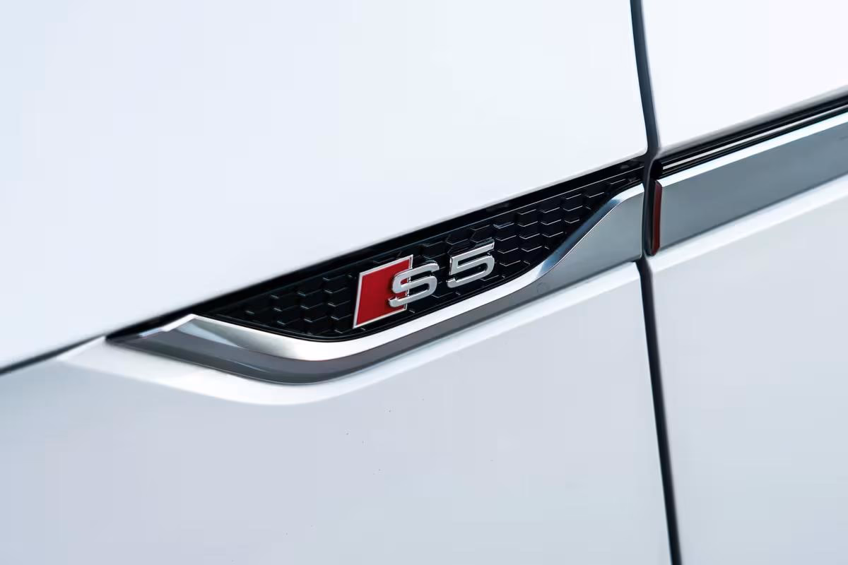 Audi: Nahaufnahme eines weißen Autos mit rotem S5-Emblem auf der Seite
