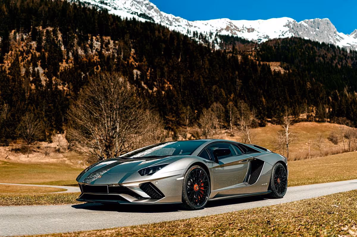 Audi: Silberner Lamborghini Aventador SVJ auf Landstraße vor schneebedeckten Bergen