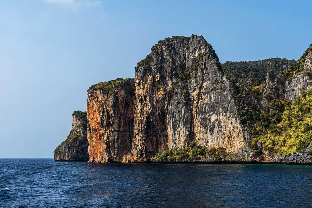 Thailand: Steile, bewachsene Felsklippe, die steil in ein ruhiges Meer abfällt.