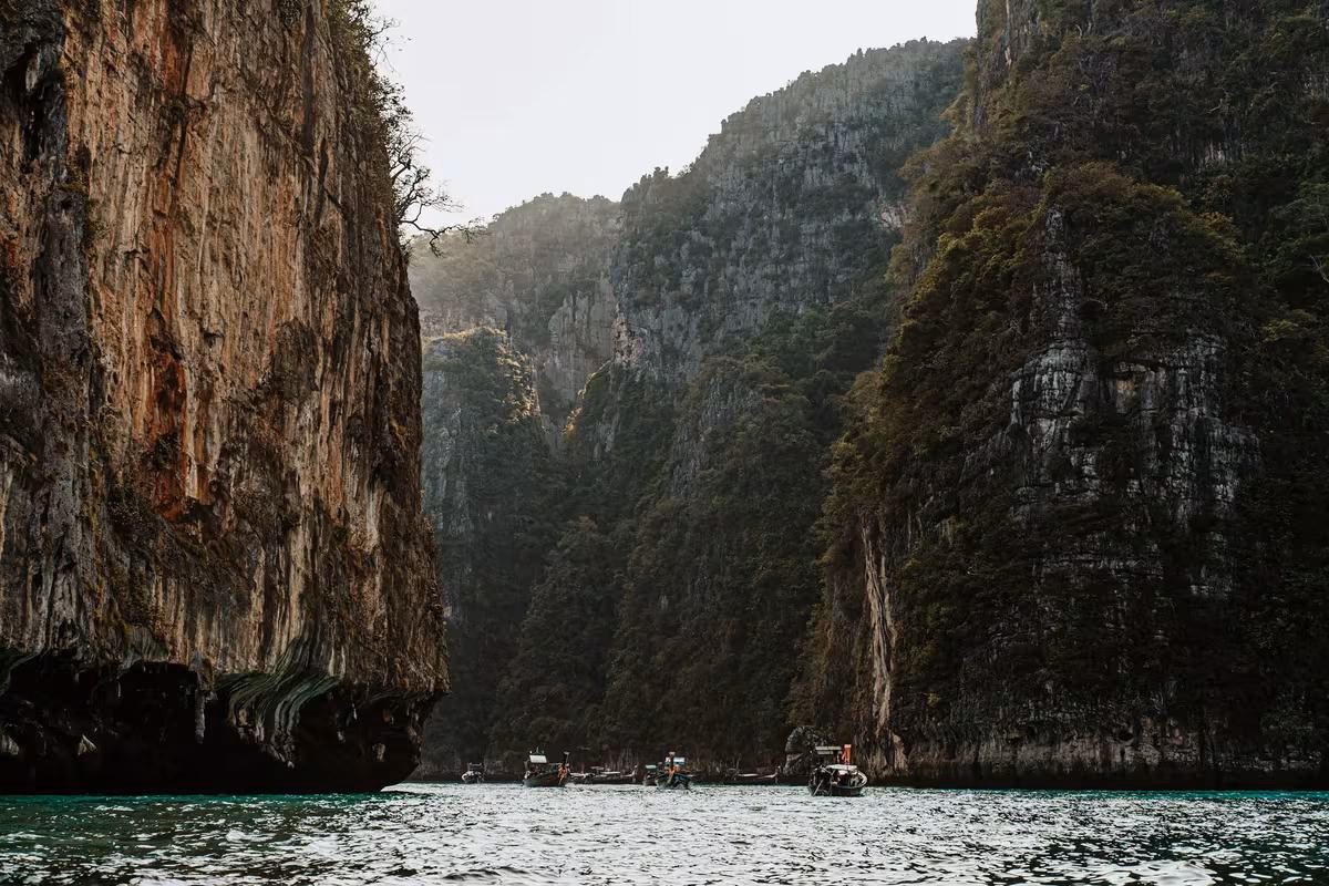 Thailand: Kalksteinklippen und Boote auf türkisfarbenem Wasser in einer thailändischen Bucht