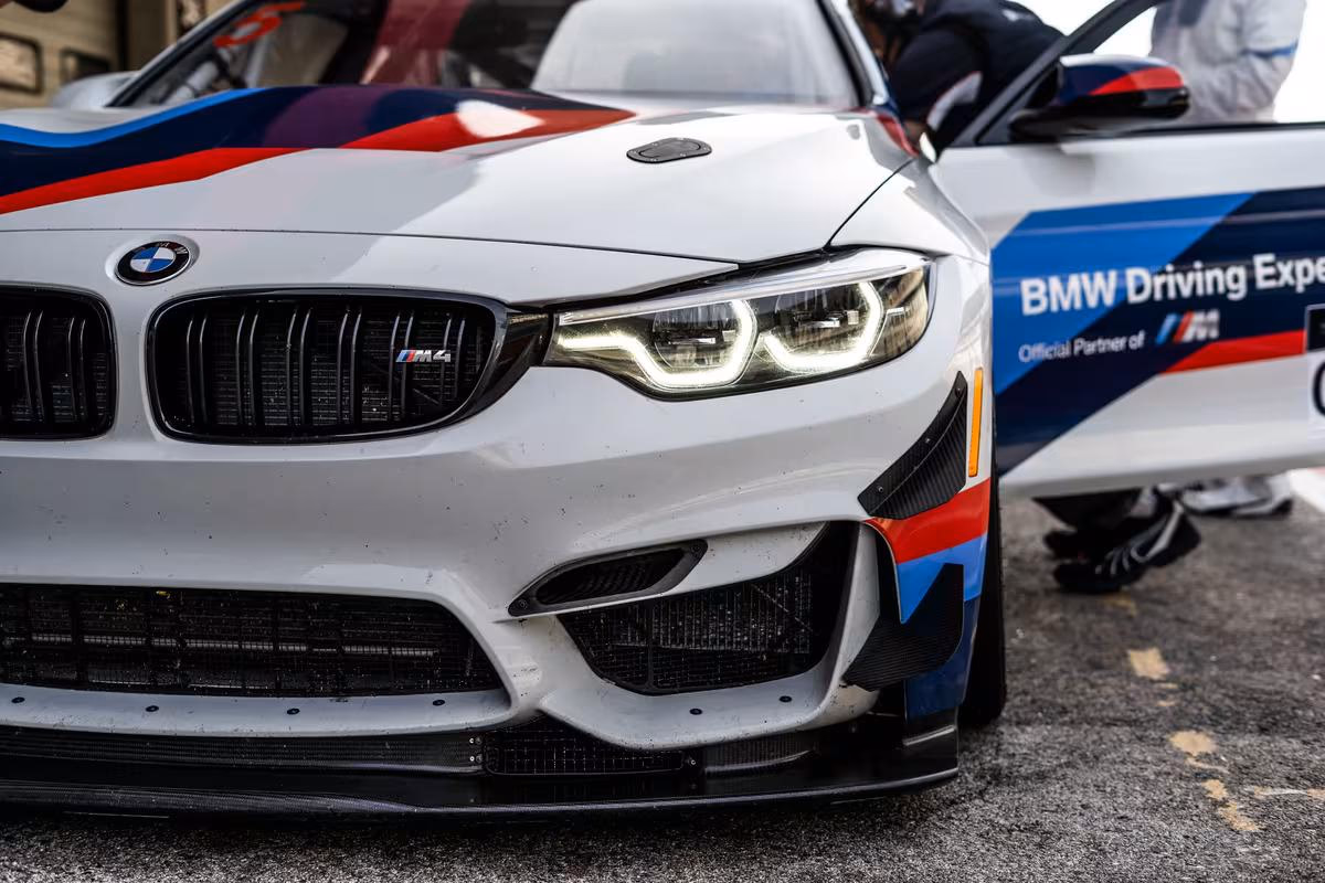 Frontansicht eines BMW M4 mit Motorsport-Lackierung und BMW Driving Experience Schriftzug.