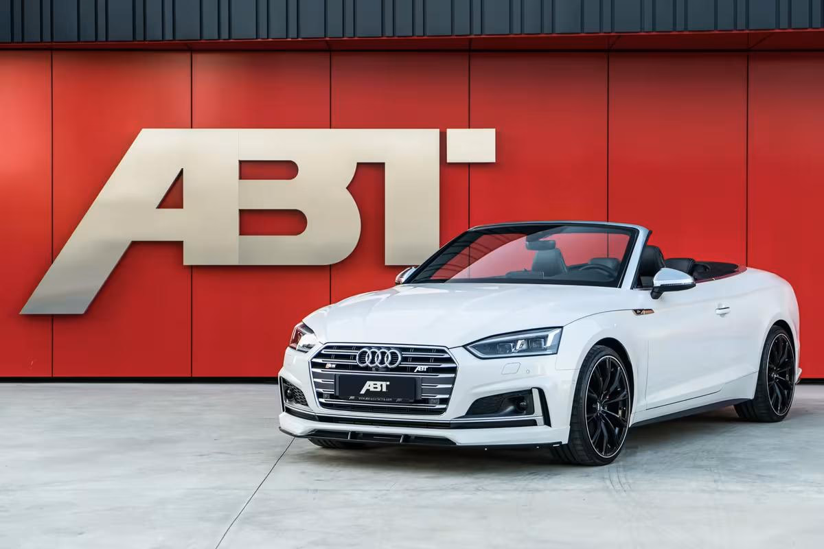 Weißer ABT Audi Cabriolet vor roter Wand mit großem ABT-Logo.