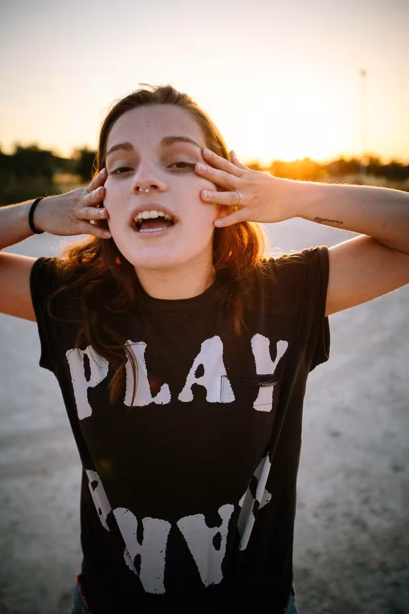 Lifestyle: Junge Frau mit schwarzem T-Shirt mit „PLAY“-Schriftzug bei Sonnenuntergang