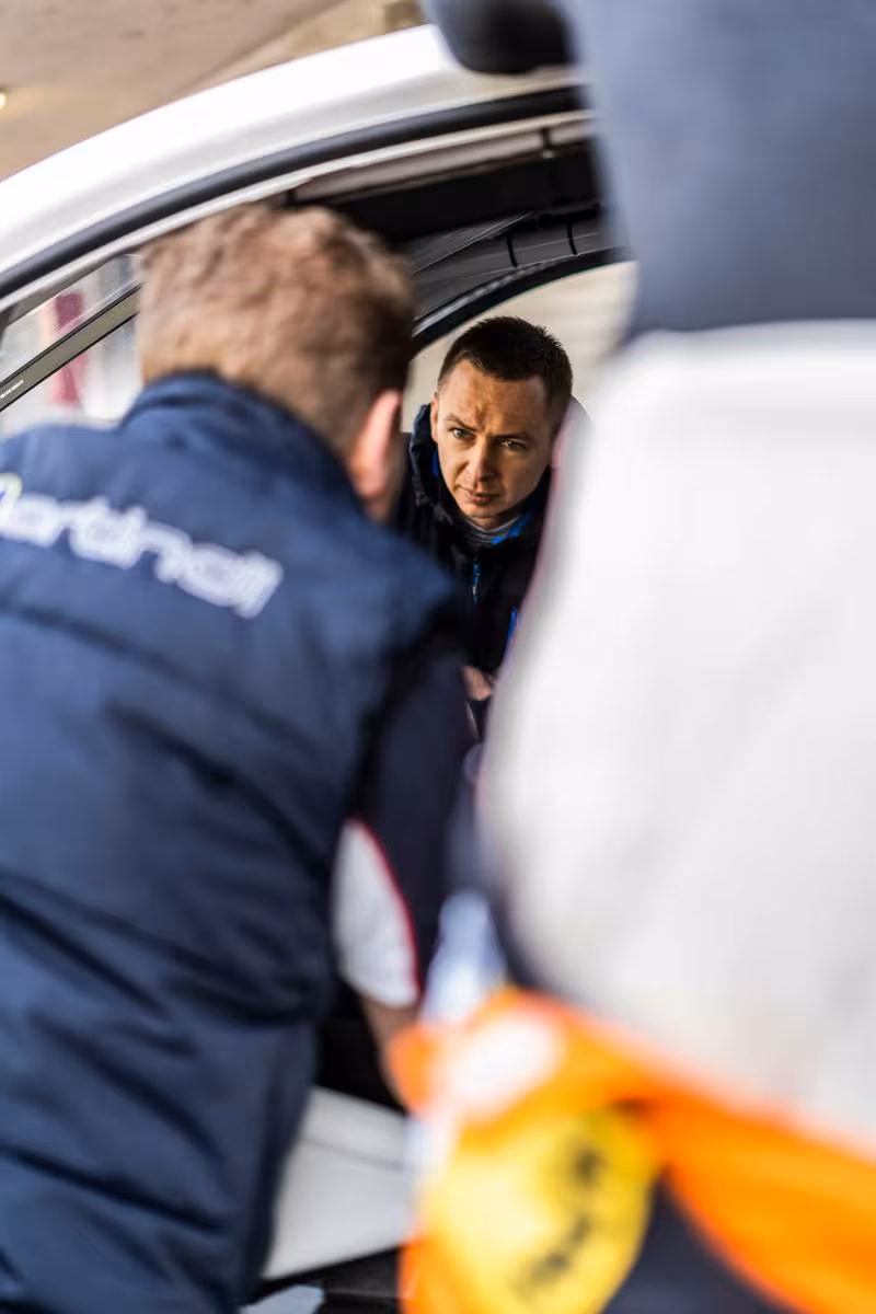 Zwei Männer in BMW-Motorsport-Teamjacken beim Austausch an einem Rennwagen.